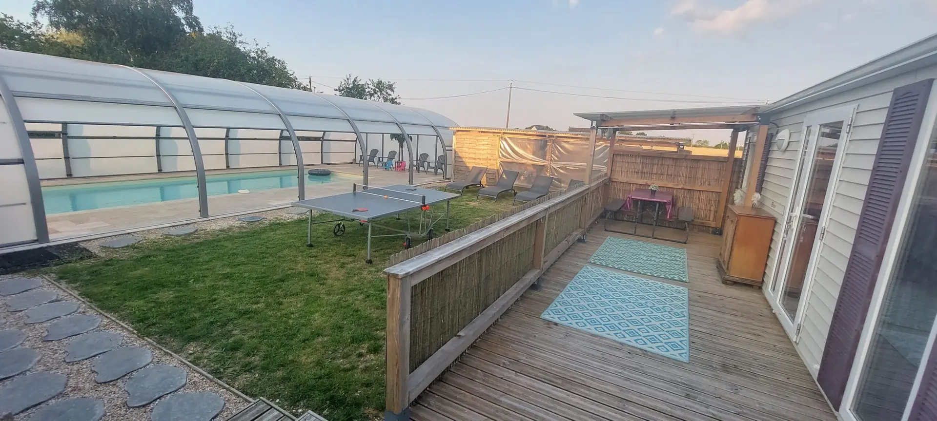 La piscine couverte, le jardin et la terrasse du mobil-home au coucher du soleil